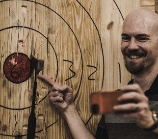 A guy pointing to the bullseye, smiling because of the axe aimed to the center